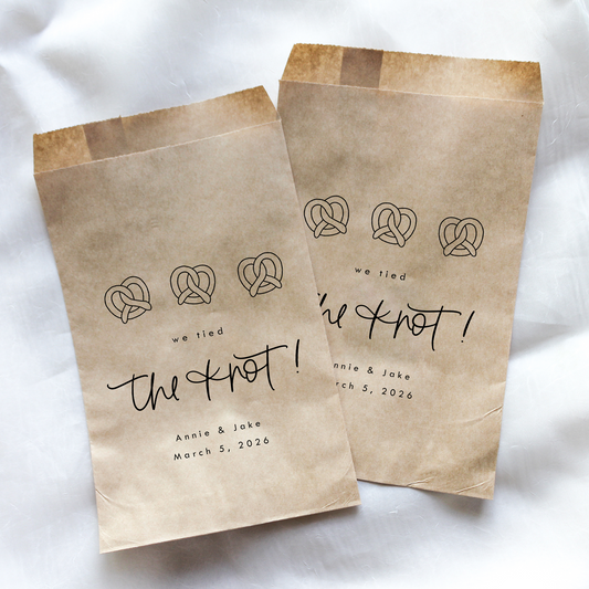 Two brown paper bags with 'we tied the knot' text and pretzel illustrations on a white background.