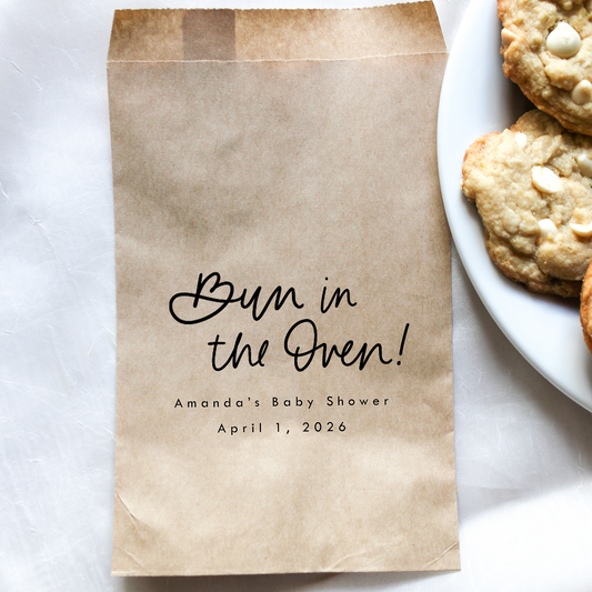 Brown paper bag with 'Bun in the Oven!' text on a white surface with cookies.