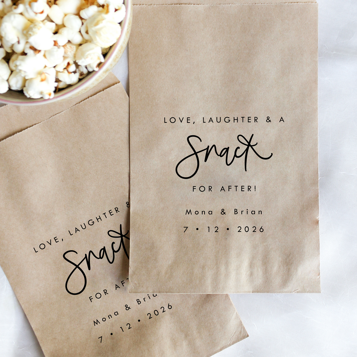 Kraft paper bags with personalized text next to a bowl of popcorn on a white background