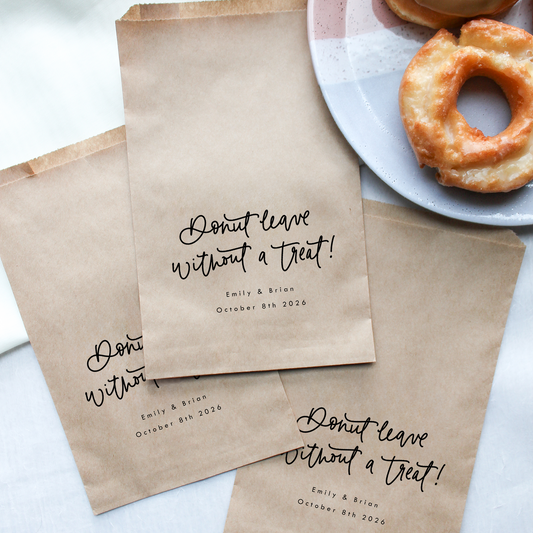 Brown paper bags with personalized text next to a plate of donuts on a light background