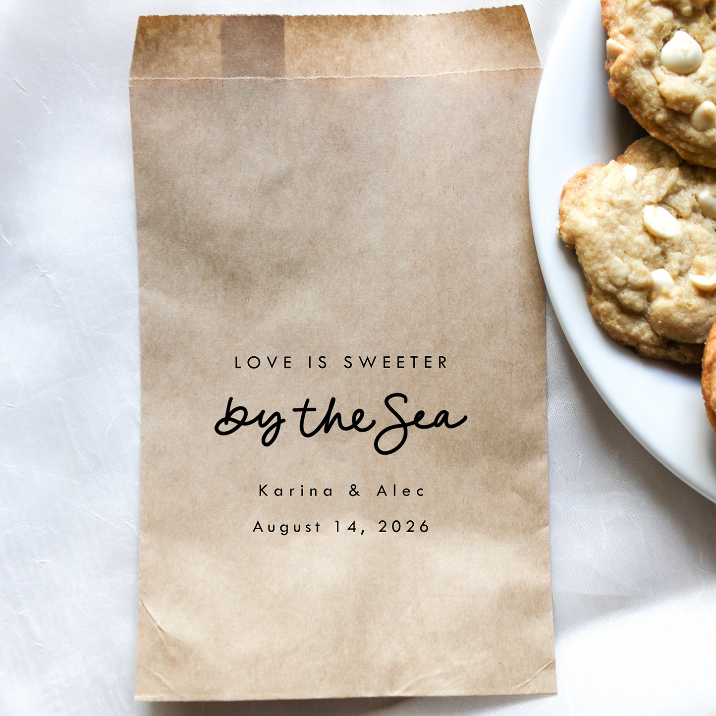 Brown paper bag with personalized text next to a plate of cookies on a white surface