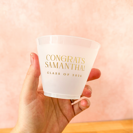 Hand holding a frosted plastic cup with 'Congrats Samantha! Class of 2026' text against a pink background