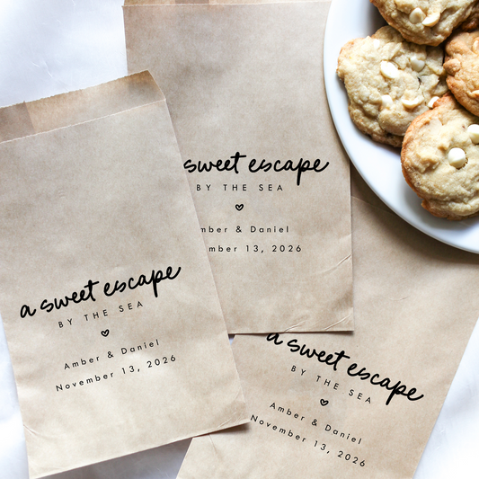 Personalized brown paper bags with 'sweet escape by the sea' text, next to a plate of cookies.