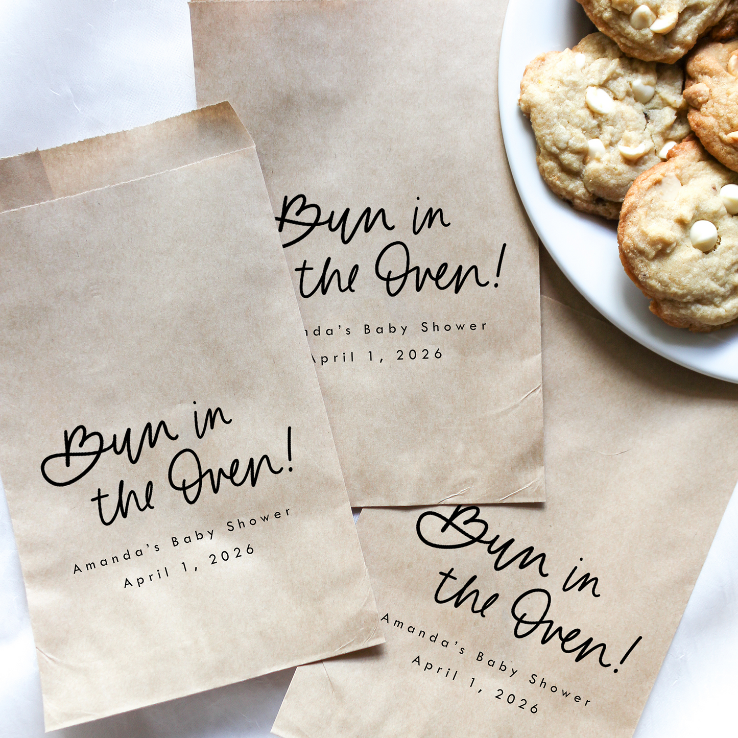 Brown paper bags with 'Bun in the Oven!' text next to a plate of cookies.