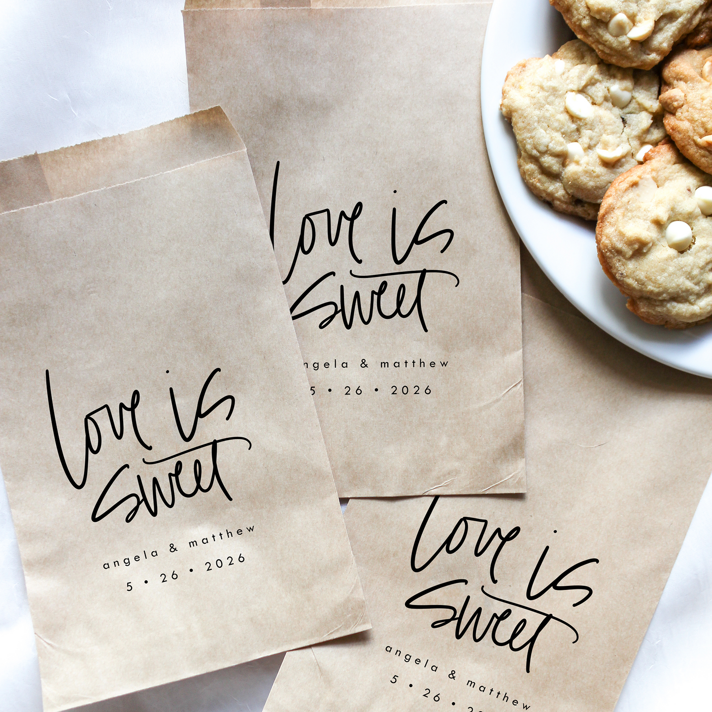 Brown paper bags with 'Love is Sweet' text on a white surface with cookies.