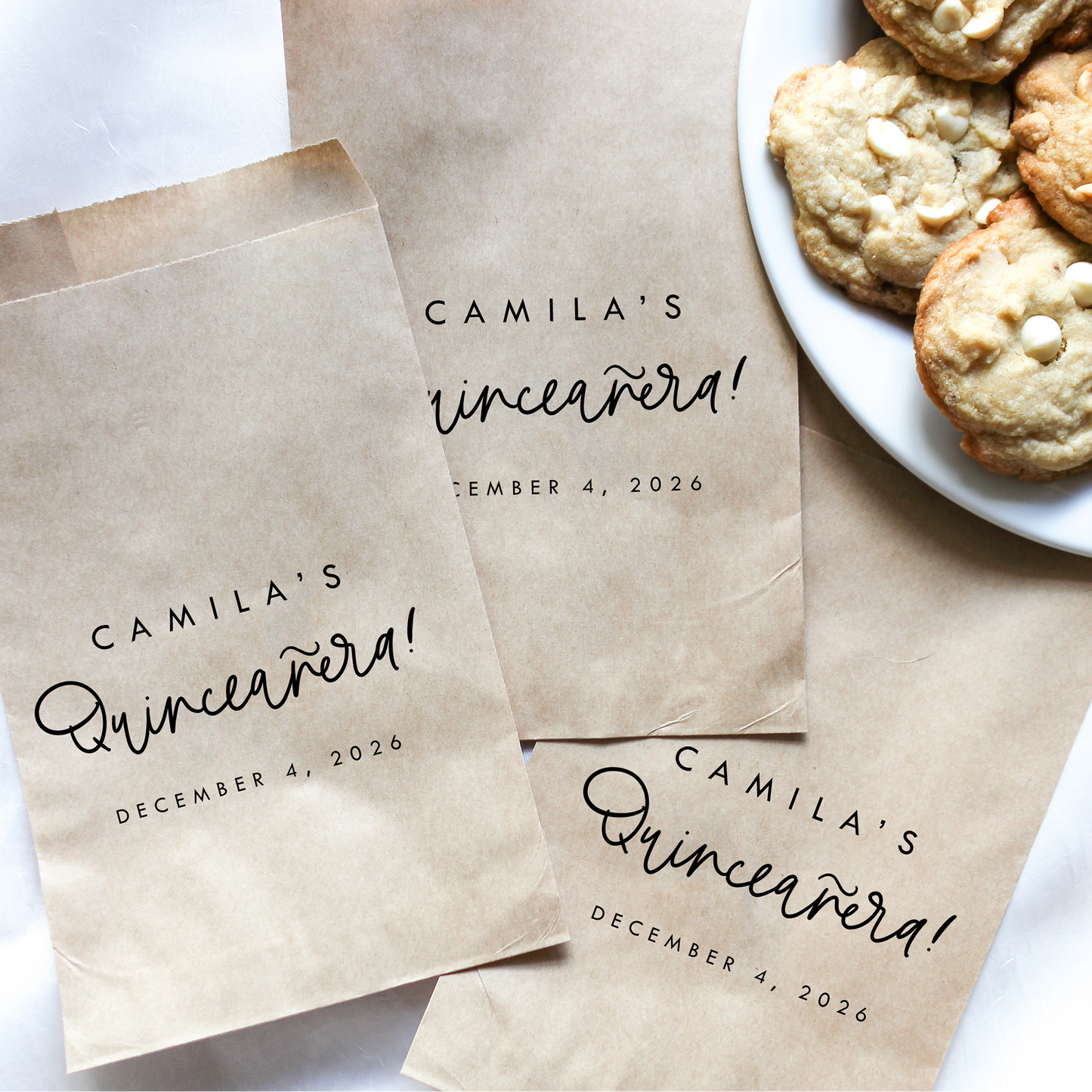 Personalized brown paper bags for Camila's Quinceanera with a plate of cookies on a white background