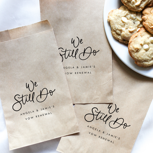 Brown paper bags with 'We Still Do' text next to a plate of cookies on a white surface