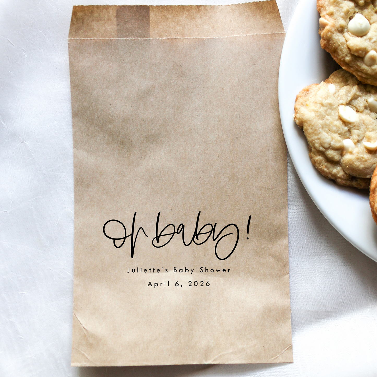 Brown paper bag with 'Oh baby!' text on a white surface with cookies.