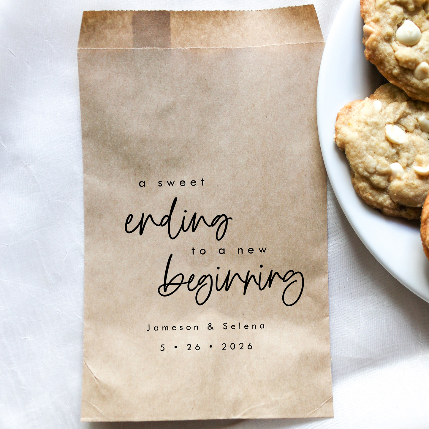 Kraft paper bag with personalized text next to a plate of cookies on a white surface