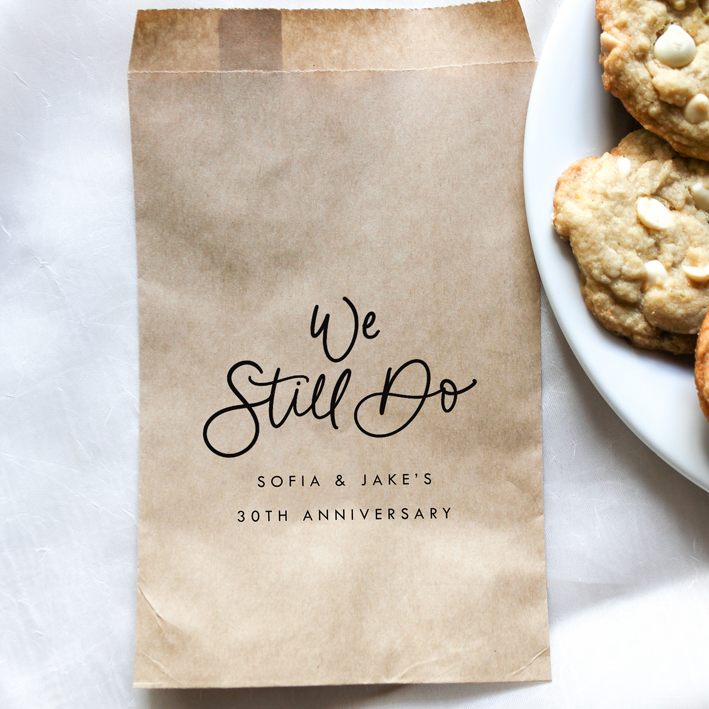Brown paper bag with 'We Still Do' text on a white surface with cookies.
