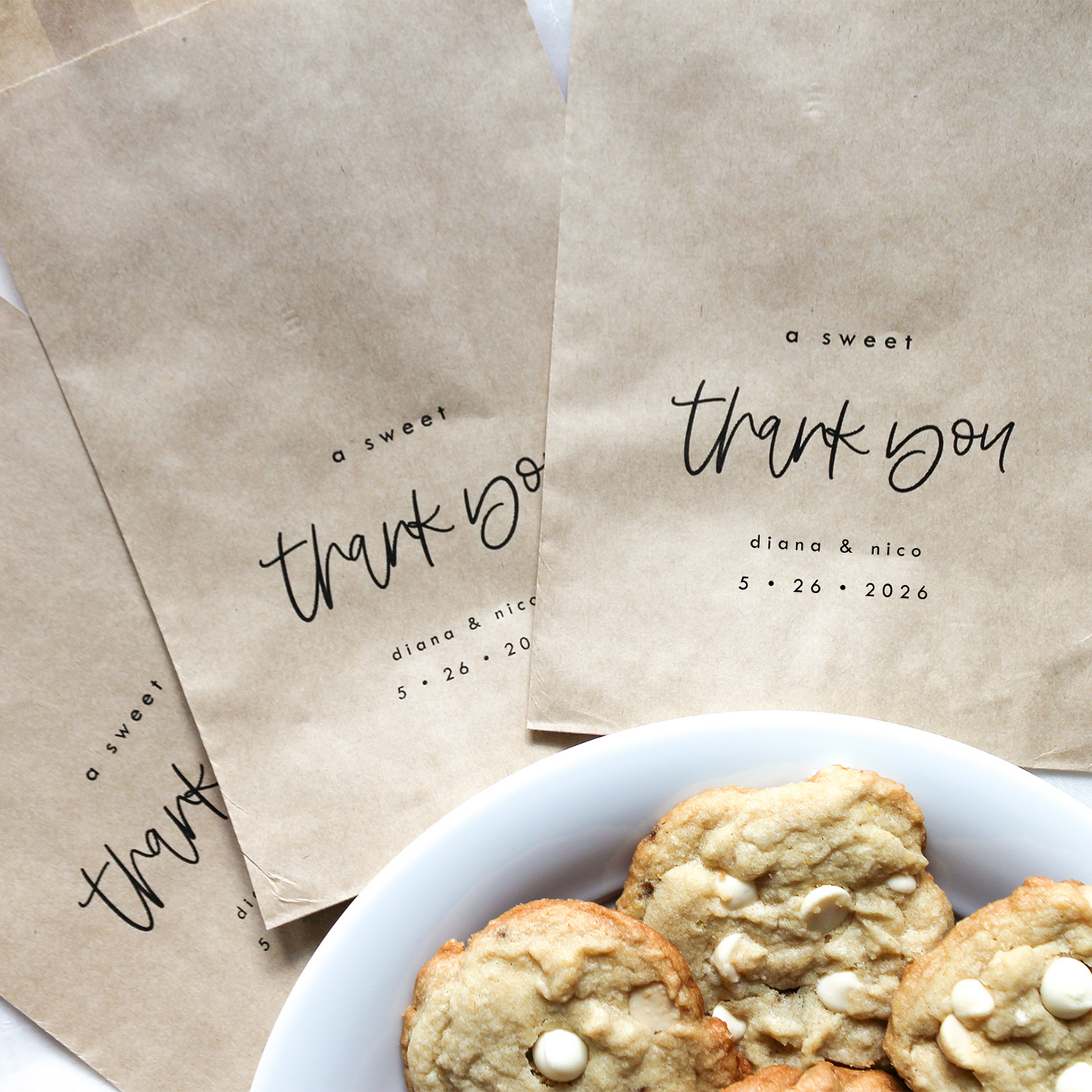 Kraft paper bags with 'thank you' text and cookies on a white surface