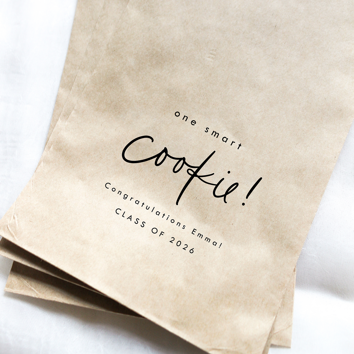 Two brown paper bags with 'one smart cookie! Congratulations Emmal Class of 2026' text on a white background