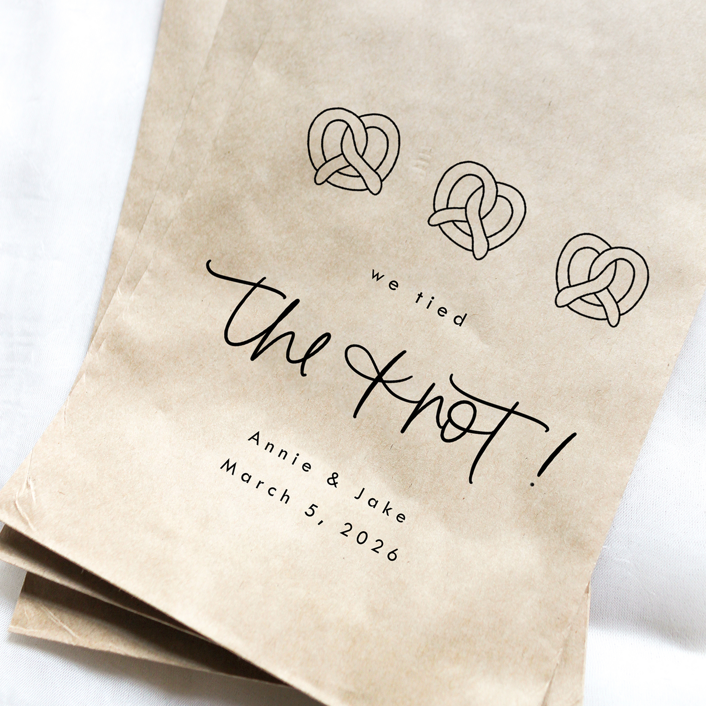 Kraft paper bags with wedding-themed pretzel design and text on a white background