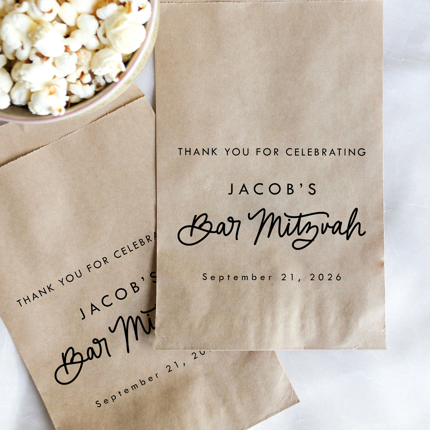 Personalized brown paper bags with 'Bar Mitzvah' text next to a bowl of popcorn on a white background