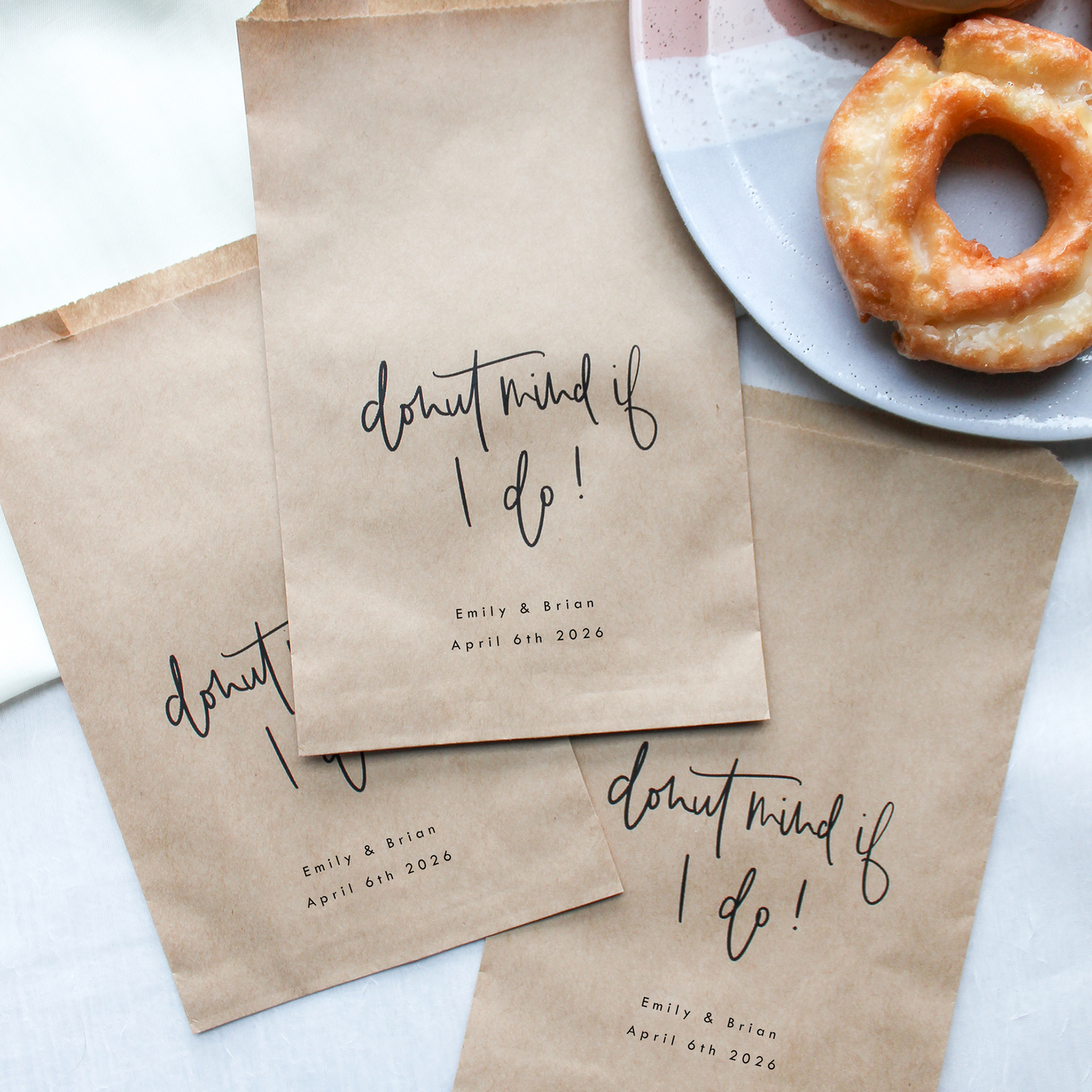 Brown paper bags with 'donut mind if I do!' text next to a plate of donuts on a light background