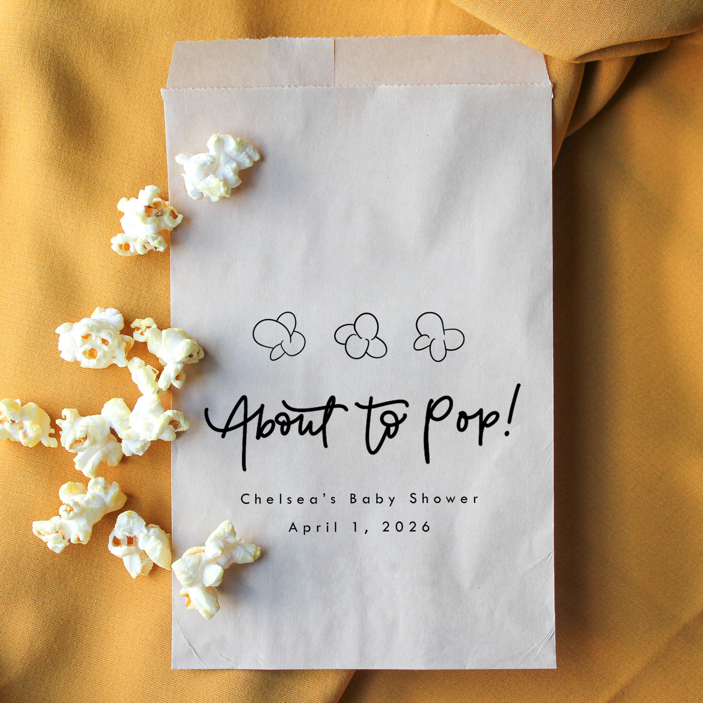 Paper bag labeled 'About to Pop!' with popcorn on a mustard yellow background