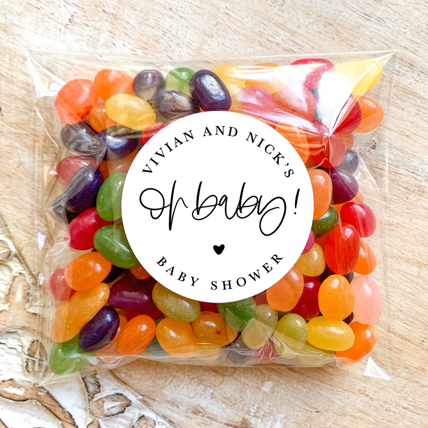 Packaged colorful jelly beans with 'Vivian and Nick's Oh Baby! Baby Shower' label on a wooden surface.