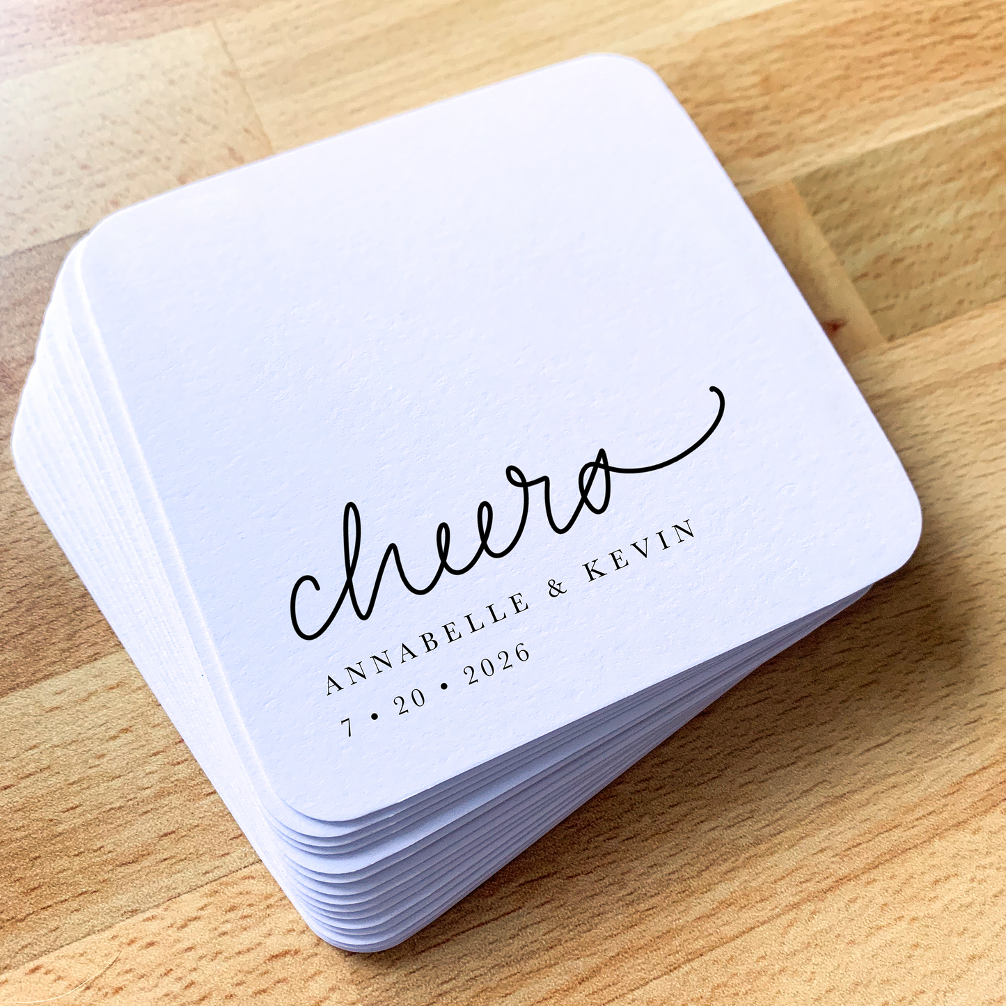 Stack of white coasters with 'cheers' branding on a wooden surface