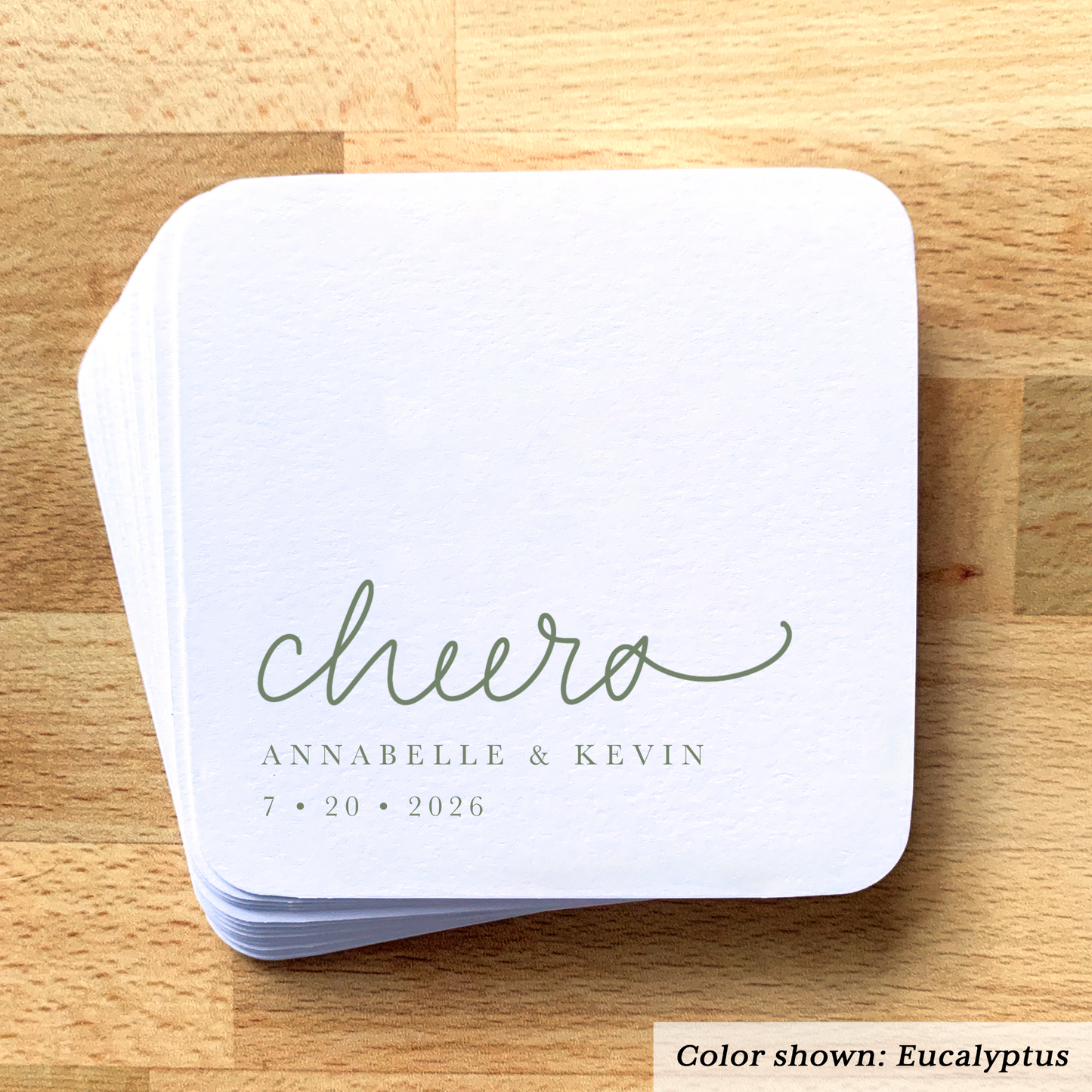 Stack of white coasters with 'cheers' and personalized text on a wooden surface