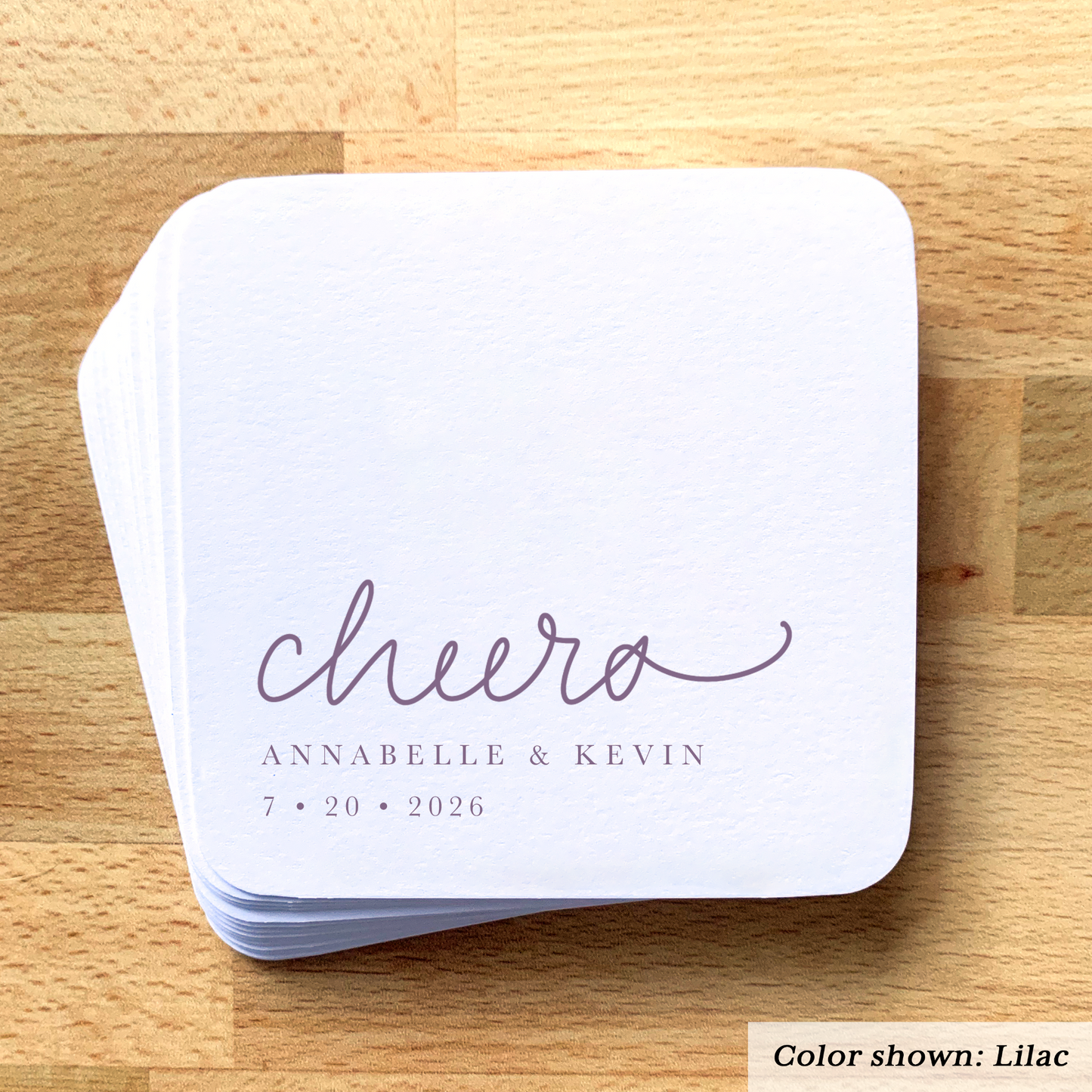 Stack of white coasters with 'cheers' and personalized text on a wooden surface