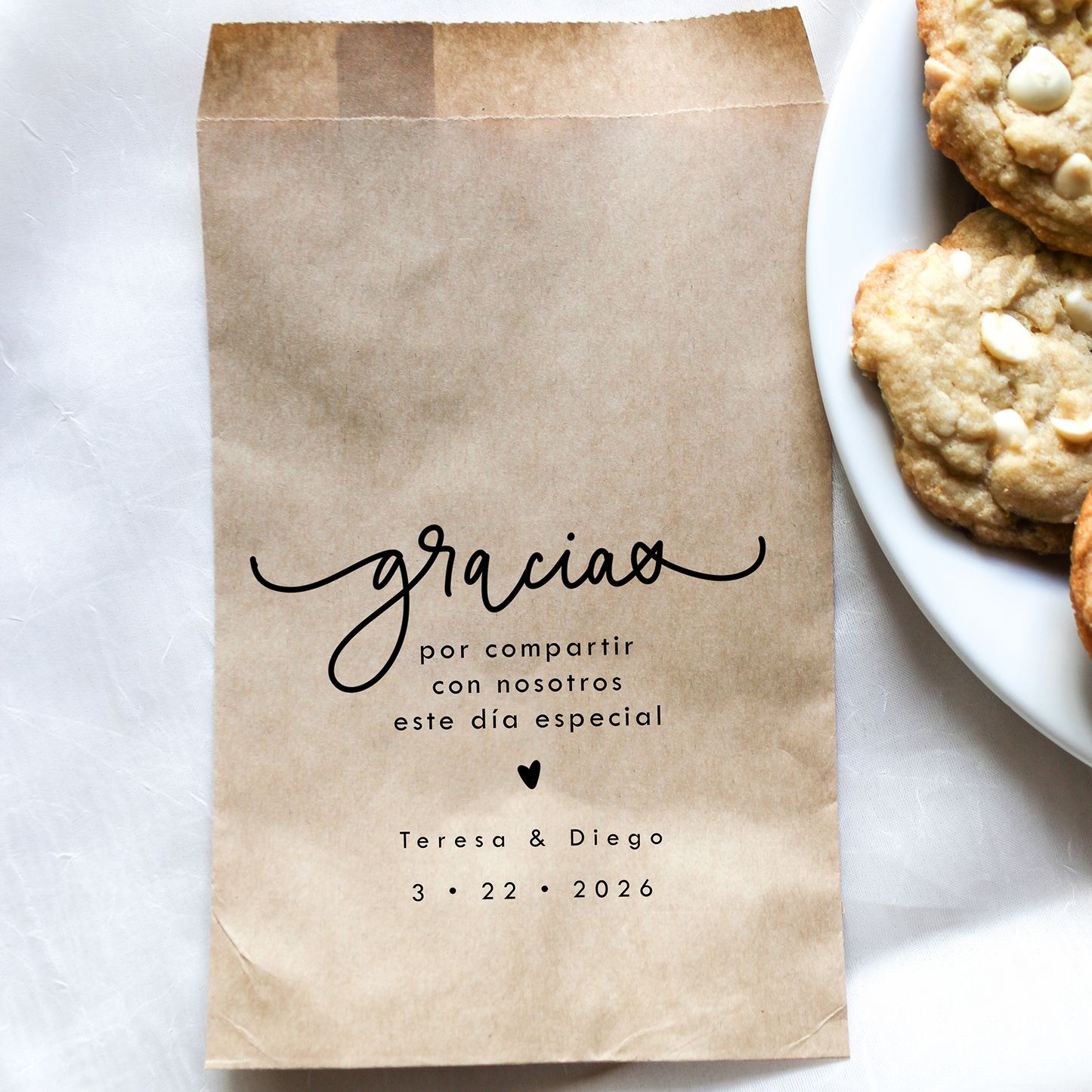 Brown paper bag with personalized text next to a plate of cookies on a white surface