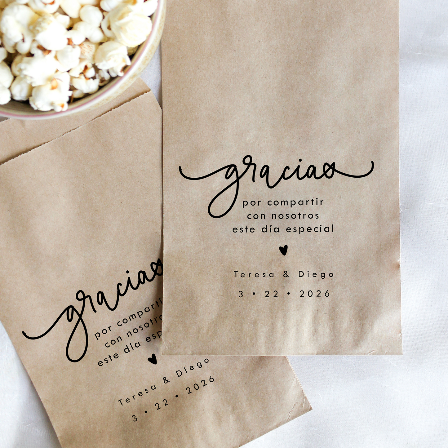 Kraft paper bags with 'gracias' text and personalized details next to a bowl of popcorn on a white background
