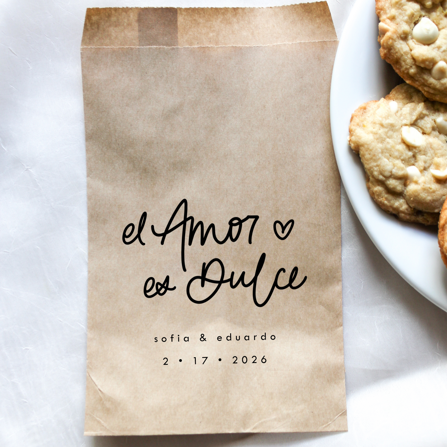 Brown paper bag with 'el Amor es Dulce' text and cookies on a white surface