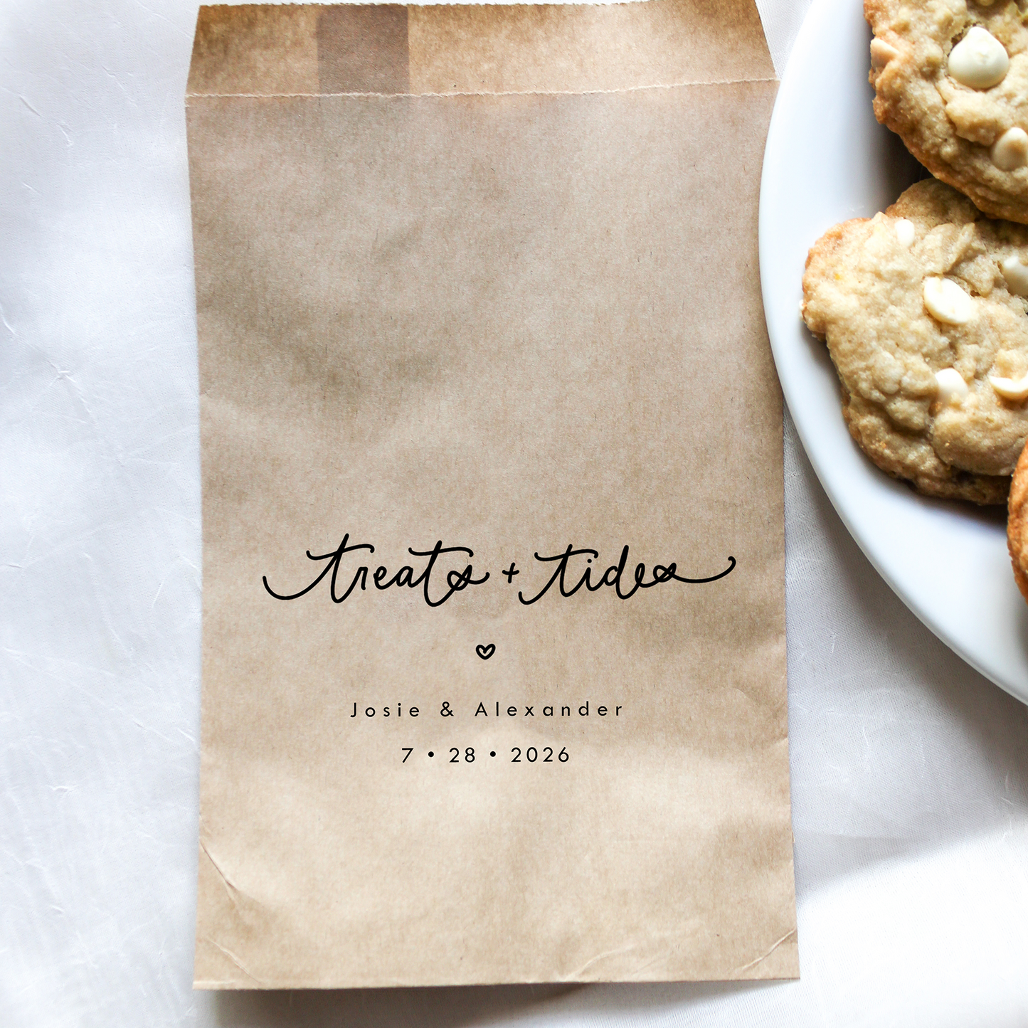 Kraft paper bag with personalized text next to a plate of cookies on a white surface